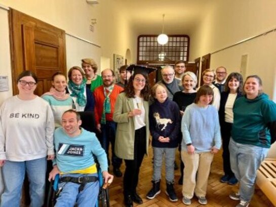 Gruppenbild von Teammitgliedern des AW-ZIB während der Feier zur bestandenen Promotion von Dr. Christina Mechler. Frau Mechler steht in der Mitte, trägt einen gebastelten schwarzen Doktorhut und lächelt in die Kamera.