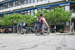 Rollstuhlfahrer und laufende Studierende vor dem Ph Gebäude.