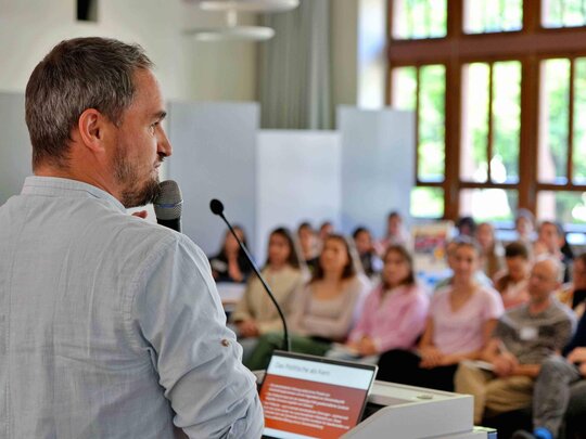 Ein Mann spricht in der Aula der Pädagogischen Hochschule Heidelberg über sein Forschungsfeld und leistet so einen Beitrag zum Transfer.