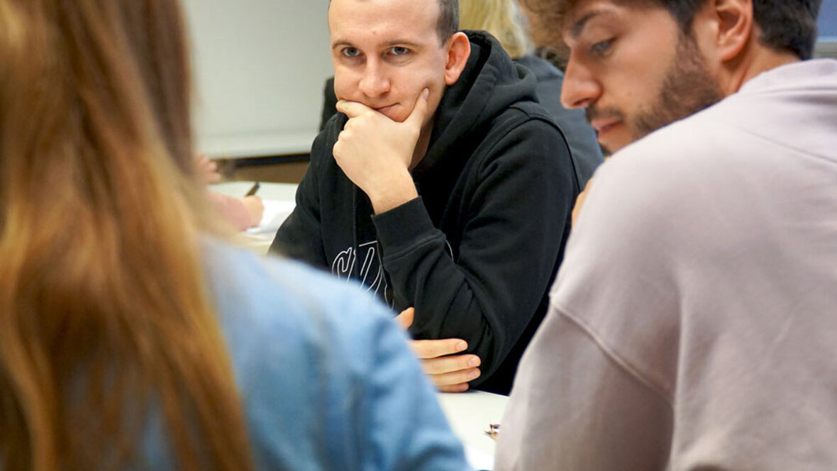 Ein Student sitzt in einem Workshop und schaut konzentriert auf die Person, deren Rücken man sieht.