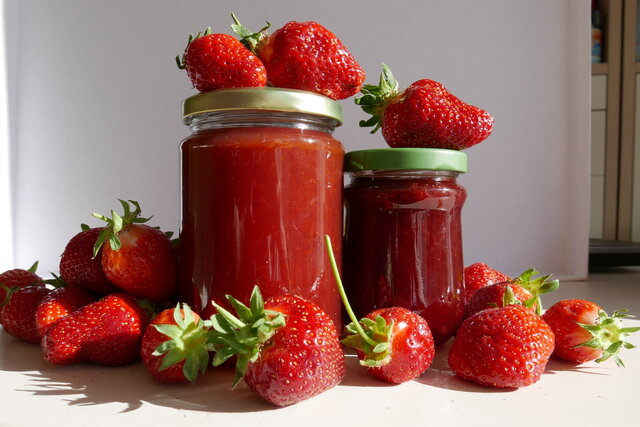 Frische Erdbeeren scharen sich um zwei Gläser mit frisch gekochter Erdbeermarmelade.