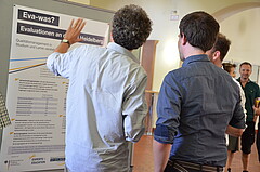 Eine kleine Gruppe von Männerns steht vor einem Poster mit der Überschrift "Eva-was?". Das Bild wurde im Foyer der Hochschule aufgenommen.