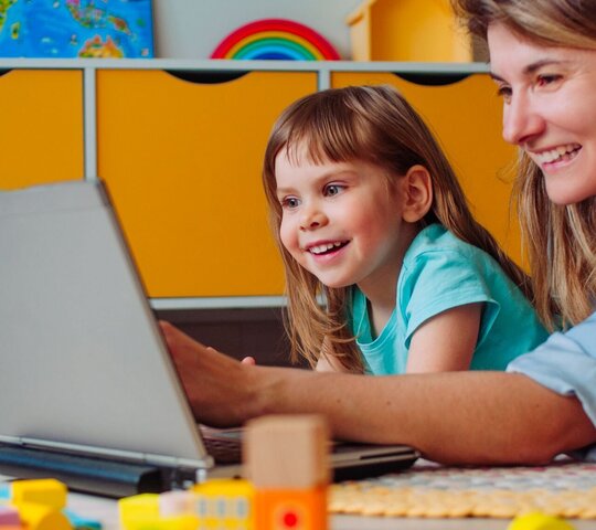 Frau und Kind liegen auf dem Bauch vor einem Laptop und schauen sich gemeinsam etwas darauf an