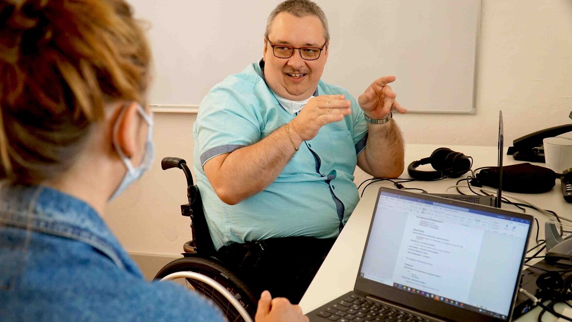 Ein Mitarbeiter der PHHD redet mit einer Frau und sitzt im Rollstuhl.