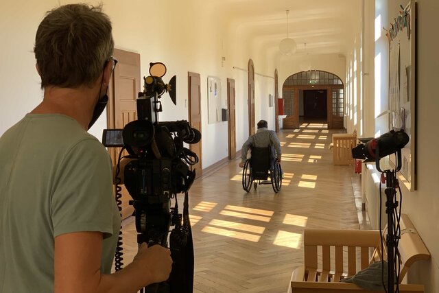 Das Foto zeigt einen Kameramann, welcher eine Bildungsfachkraft im Rollstuhl filmt.