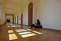 Das Symbolbild zeigt ein junges Mädchen, das im leeren Flur der Hochschule auf dem Boden sitzt und auf ihr Handy schaut. Copyright: Pädagogische Hochschule Heidelberg