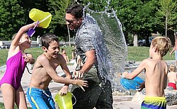 Kinder die sich gegenseitig und einem jungen Mann Wasser überschütten.