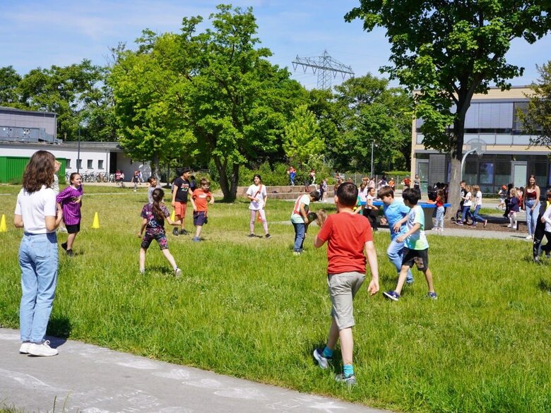 Das Bild zeigt eine Gruppe von Kindern, die sich draußen auf einer grünen Wiese bewegen