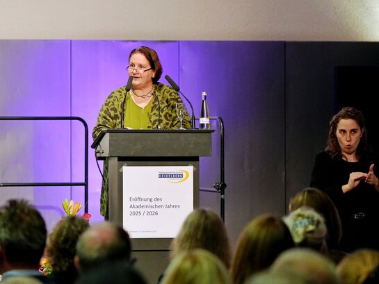 Ministerin Schopper bei der Festrede zur Eröffnung des Akademischen Jahres der Pädagogischen Hochschule Heidelberg. Neben ihr steht eine Frau, die die Rede in Gebärdensprache übersetzt.