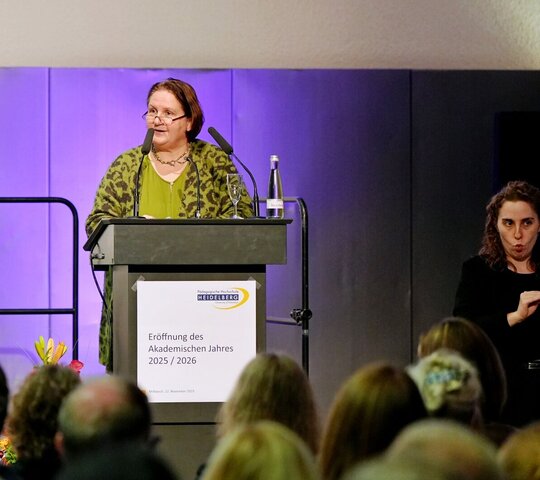 Ministerin Schopper bei der Festrede zur Eröffnung des Akademischen Jahres der Pädagogischen Hochschule Heidelberg. Neben ihr steht eine Frau, die die Rede in Gebärdensprache übersetzt.