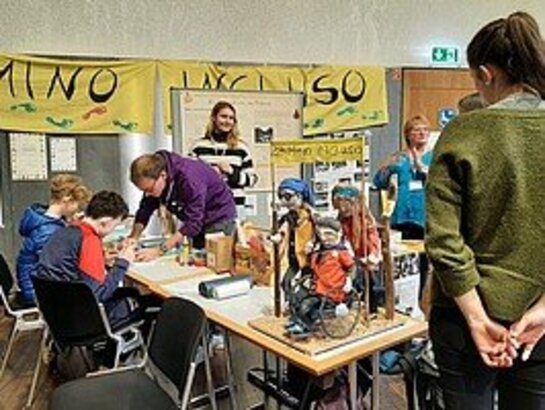 Das Bild zeigt Besucher:innen der Lernortmesse, die sich ausgestellte Materialien auf einem Tisch ansehen.