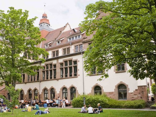 Das Foto zeigt den Innenhof des Altbaues. Auf der Wiese liegen und sitzen einige Studierende.