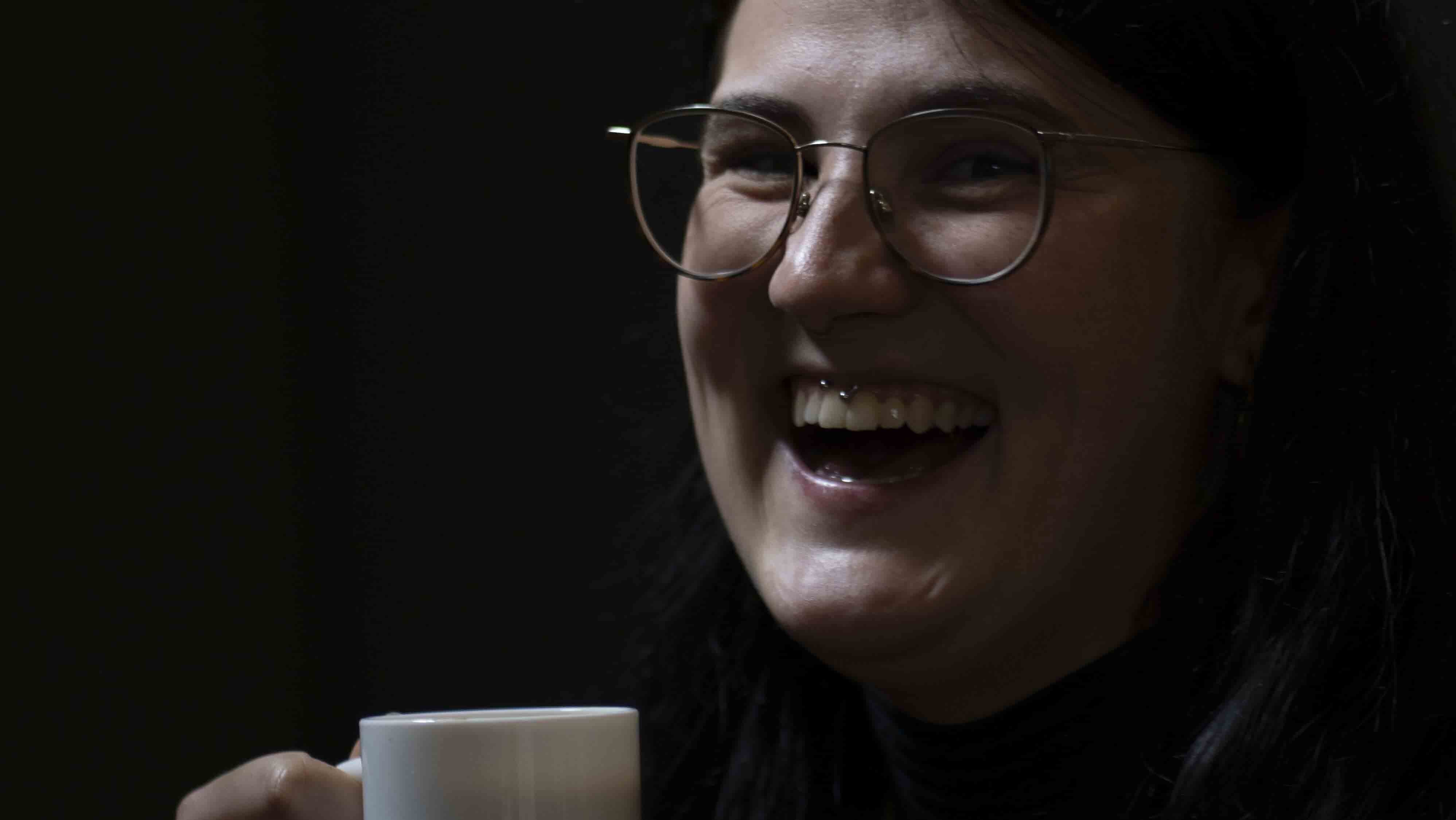 Das Bild zeigt eine Frau, die eine Kaffeetasse in der Hand hält. Die Frau lacht.