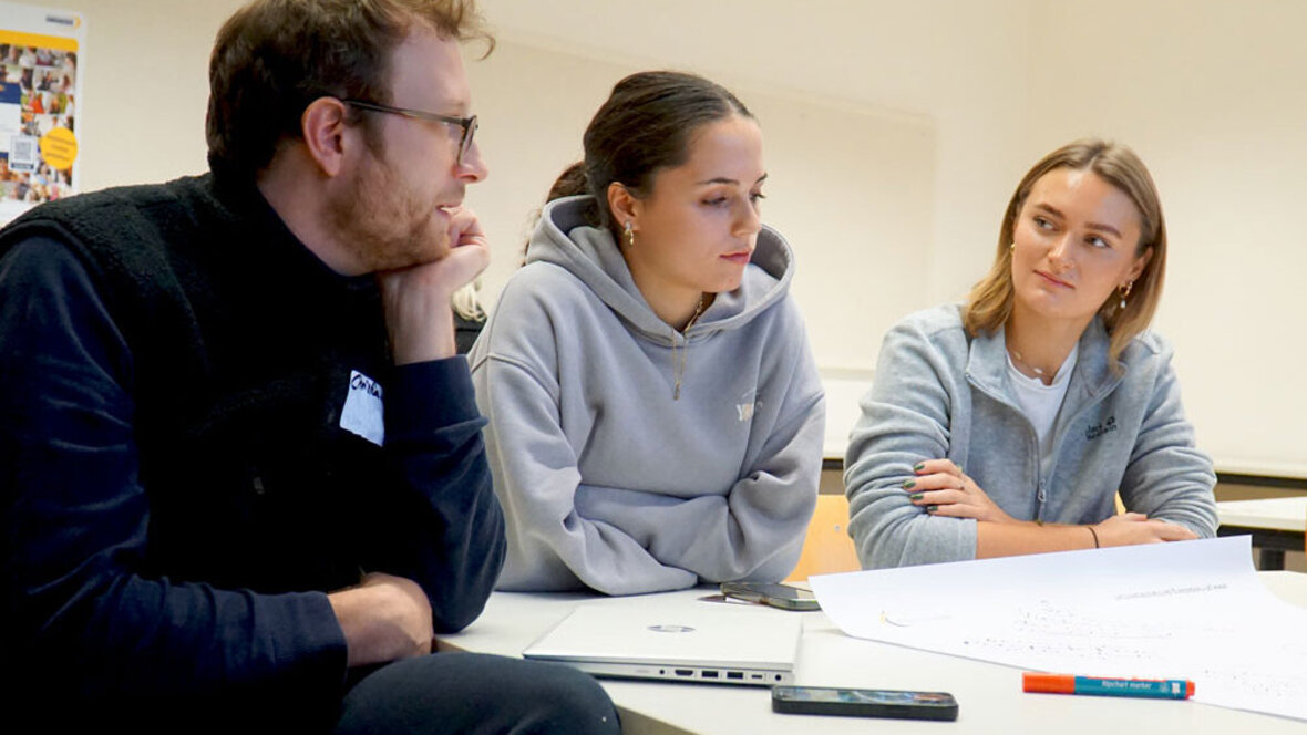 Ein junger Mann und zwei junge Frauen arbeiten in einem Workshop zusammen.