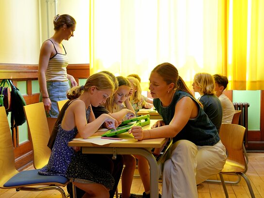 Das Foto zeigt eine Schulklasse in kleinen Gruppen gemeinsam arbeiten.