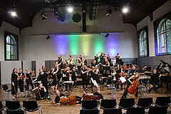 Das Bild zeigt das Hochschulorchester auf der Bühne in der Mehrzweckhalle im Altbau.