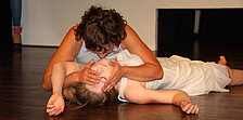 Szene von Theateraufführung, Person hält das Gesicht von auf dem Boden liegender Person