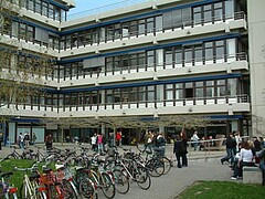 Das Bild zeigt den Neubau der Pädagogischen Hochschule Heidelberg von außen. Davor stehen zahlreiche Fahrräder und Personen.