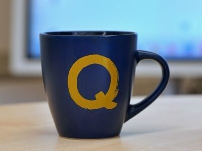 Eine Tasse im Blau der Pädagogischen Hochschule auf die in Q im Gelb der Pädagogischen Hochschule gedruckt ist. Das Q steht für Qualitätsmanagement.