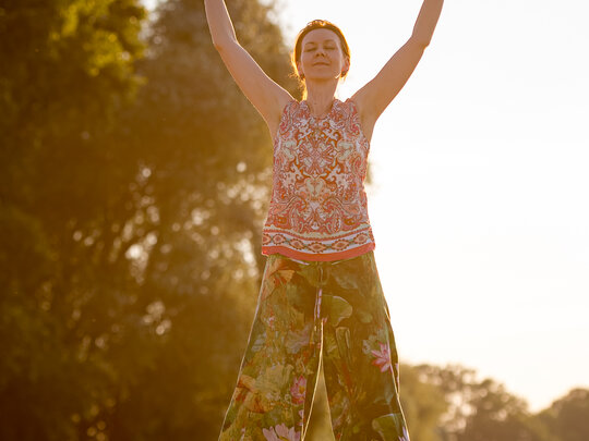 Person macht Qigong auf einem Feld, Sonnenstrahlen im Hintergrund