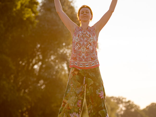 Person macht Qigong auf einem Feld, Sonnenstrahlen im Hintergrund