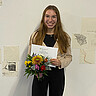 Das Bild zeigt Anna Morawietz. Sie hält die Auszeichnung sowie einen Blumenstrauß in der Hand. Sie strahlt in die Kamera.