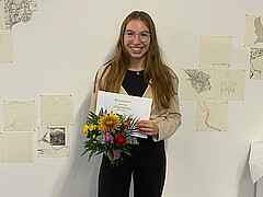 Das Bild zeigt Anna Morawietz. Sie hält die Auszeichnung sowie einen Blumenstrauß in der Hand. Sie strahlt in die Kamera.