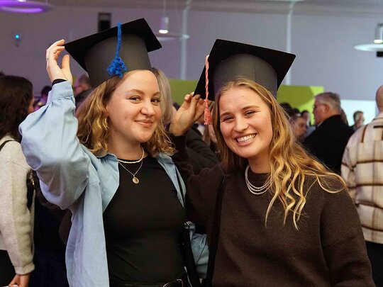 Zu sehen sind zwei Alumni der PHHD mit selbstgebasteltem Graduiertenhut.