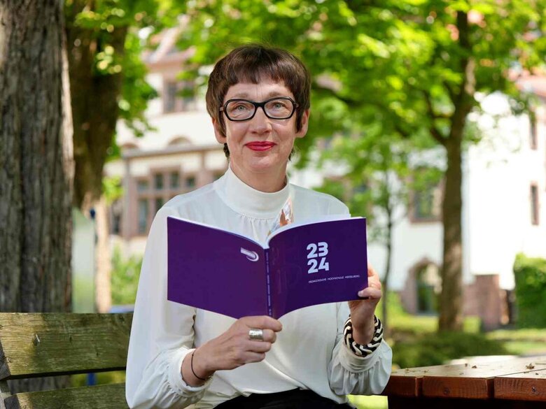Die Rektorin Frau Vach sitzt im Innenhof der Pädagogischen Hochschule mit dem aktuellen Jahresbericht in der Hand.