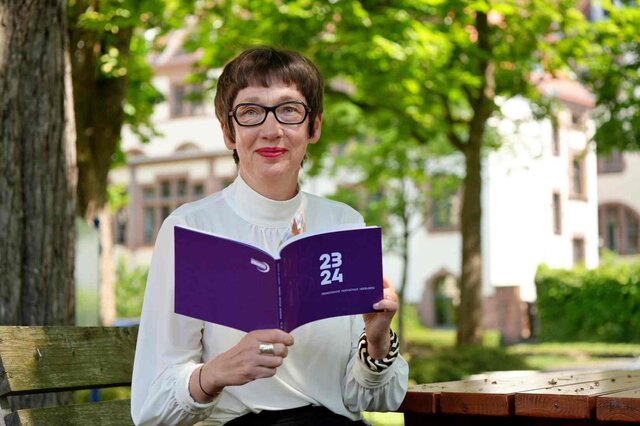 Die Rektorin Frau Vach sitzt im Innenhof der Pädagogischen Hochschule mit dem aktuellen Jahresbericht in der Hand.