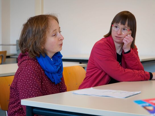 Das Bild zeigt die Qualifizierungsteilnehmerinnen Louisa Kabbe und Susann Bensch im Gespräch. Sie sitzen an einem Tisch