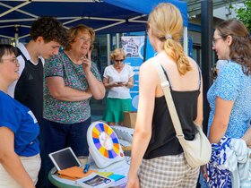 Das Bild zeigt den Stand des AW-ZIB im Rahmen der PH Days. Interessierte Stuudierende stehen vor dem Stand, der von MIigliedern des AW-ZIB und der Fachschaft Sonderpädagogik betreut wird. Auf einem runden Tisch steht ein barrierearmes Glücksrad, das mit einem Buzzer bedient werden kann.