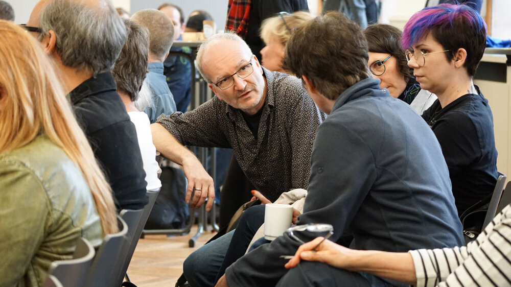 Blick ins Publikum während des hochschulweiten Workshops. Die Menschen unterhalten sich.