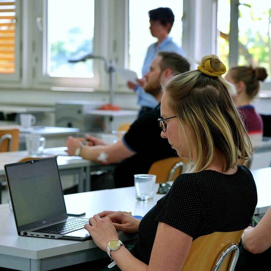 Studierende sitzen an Tischen während eines Vortrages.