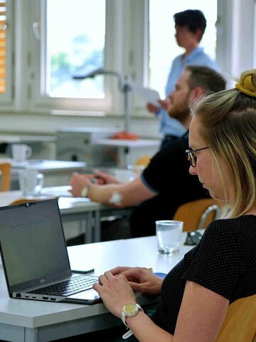 Studierende sitzen an Tischen während eines Vortrages.