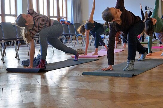 Abgebildet sind Menschen beim Yoga in der Altbau-Aula