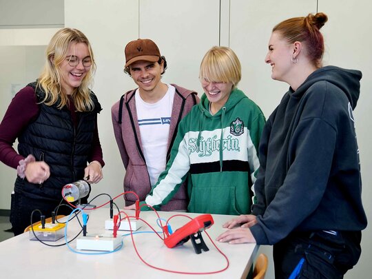 Drei Studentinnen und ein Student stehen um einen Tisch auf dem ein physikalischer Versuch aufgebaut ist.