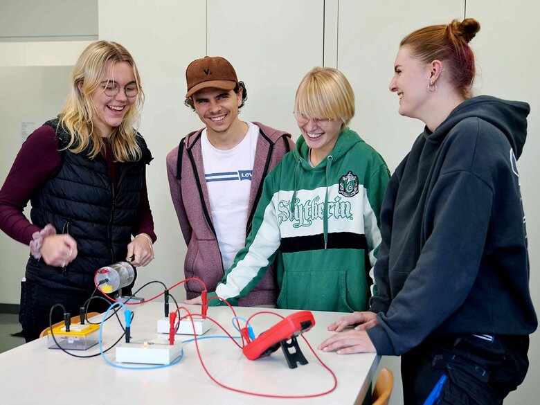 Drei Studentinnen und ein Student stehen um einen Tisch auf dem ein physikalischer Versuch aufgebaut ist.
