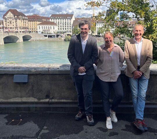 Foto der drei Lehrenden vor dem Hintergrund des Flusses und der Gebäude