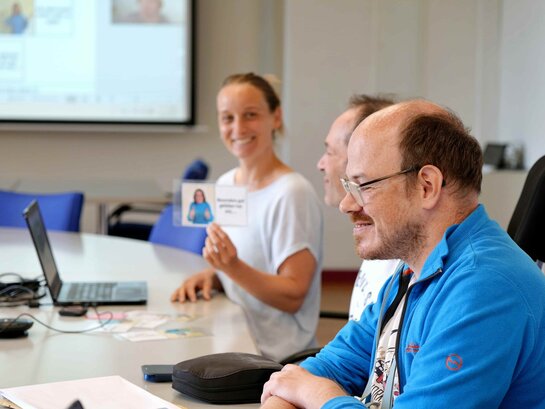 Das Bild zeigt eine Situation aus dem Forschungsplenum: Seitenaufnahme von Bildungsfachkraft Thilo Krahnke, im Hintergrund ist Kathrin Ludwig, die zur Promotion abgeordnet ist. Sie hält eine Karte in der Hand. 