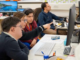 Die vier Qualifizierungsteilnehmer:innen sitzen vor einem Computer-Bildschirm. Lilly Lorenz zeigt auf den Bildschirm.