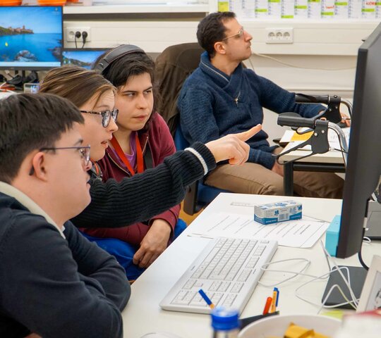 Die vier Qualifizierungsteilnehmer:innen sitzen vor einem Computer-Bildschirm. Lilly Lorenz zeigt auf den Bildschirm.
