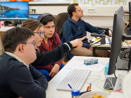 Die vier Qualifizierungsteilnehmer:innen sitzen vor einem Computer-Bildschirm. Lilly Lorenz zeigt auf den Bildschirm.