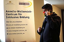 Das Bild zeigt Herrn Dr. Klemens Ketelhut beim telefonieren vor einem Informationsplakat der AW-ZIB. Copyright Pädagogische Hochschule Heidelberg