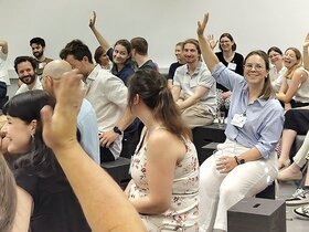 Teilnehmende an der Auftakt- und Vernetzungsveranstaltung des PH-übergreifenden Mentoringprogramms m.powerment sitzen zusammen. Einige heben die Hand. Die Stimmung scheint locker zu sein.