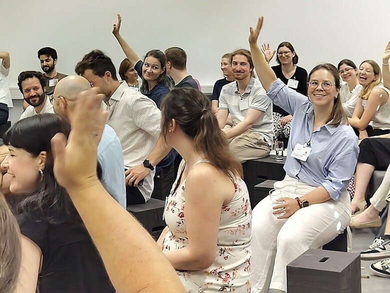 Teilnehmende an der Auftakt- und Vernetzungsveranstaltung des PH-übergreifenden Mentoringprogramms m.powerment sitzen zusammen. Einige heben die Hand. Die Stimmung scheint locker zu sein.