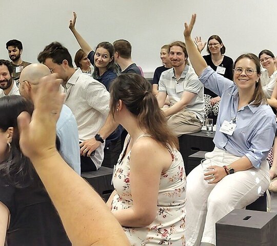 Teilnehmende an der Auftakt- und Vernetzungsveranstaltung des PH-übergreifenden Mentoringprogramms m.powerment sitzen zusammen. Einige heben die Hand. Die Stimmung scheint locker zu sein.