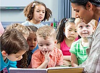 Das Bild zeigt eine Frau, die mehreren Kindern etwas vorliest.
